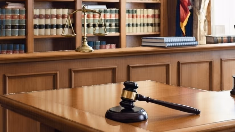 Wooden judge’s gavel resting on a polished table with brass scales and law books in the background.