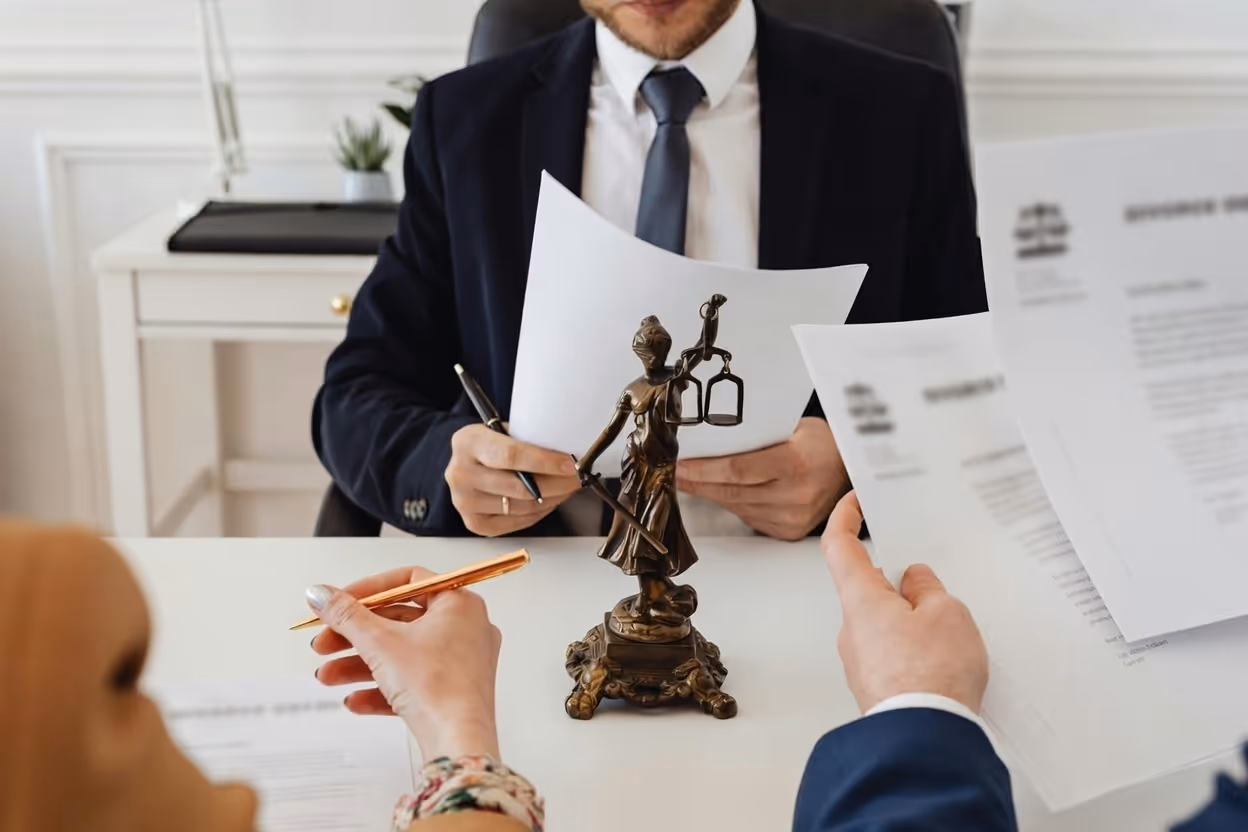 Lawyer and clients reviewing legal documents with a Lady Justice statue on the desk.