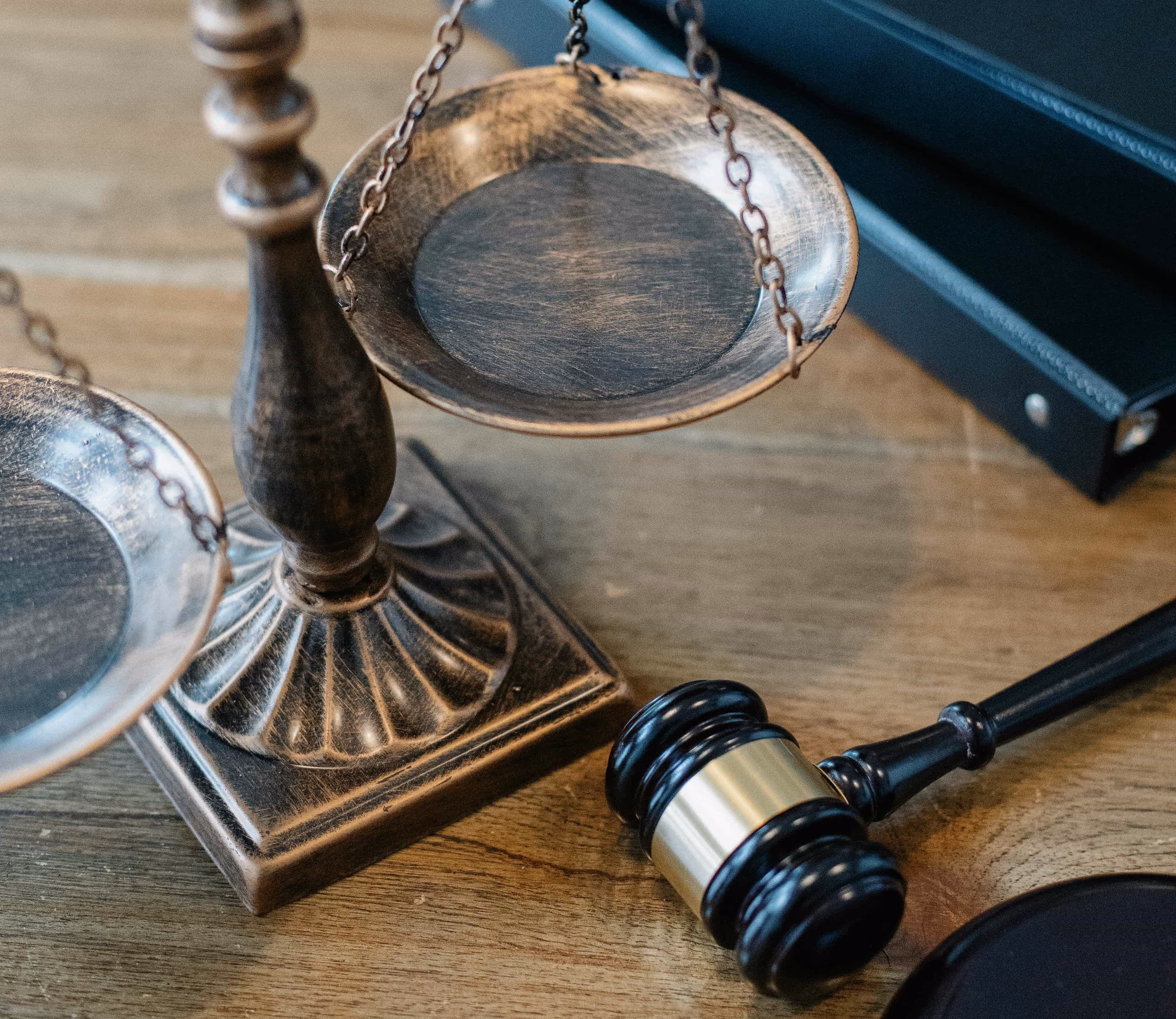 Close-up of a brass balance scale and a black wooden judge's gavel on a wooden surface.